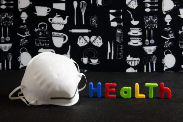 A white safety mask with multicoloured children's letters spelling "health" on a black and white background.