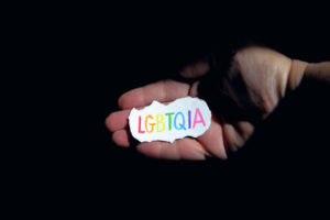 A hand holding a small sign that reads in rainbow colours: LGBTQIA